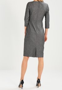 Grå, figursydd klänning med trekvartslånga ärmar, sömdetalj bak och knälång längd. Buren med svarta högklackade skor.