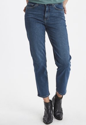 Jeans in denim blu scuro con taglio dritto, design a cinque tasche, trama sbiadita e risvolti arrotolati, abbinati a stivaletti neri alla caviglia.