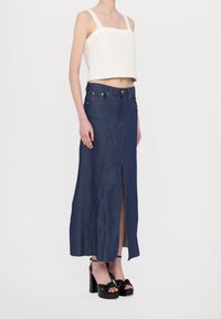 Witte crop top met een gestructureerd breipatronen, gecombineerd met een hoog getailleerde, donkerdenim maxi-rok met een voorkantsplit en duidelijke naden.