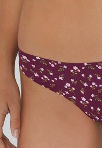 Bordowy dół od bikini z kwiecistym wzorem, w którym znajdują się małe różowe kwiaty i zielone liście; teksturowany materiał i umiarkowany krój.