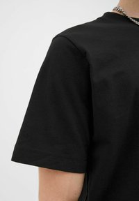 Schwarzes Baumwoll-T-Shirt mit kurzen Ärmeln. Hat einen runden Halsausschnitt und einen geraden Saum. Glatte Textur mit minimalen Nähten.
