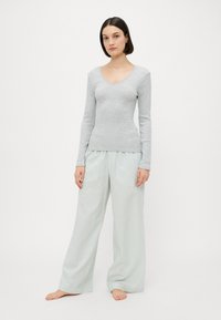 Haut à manches longues gris clair avec un col en V ; associé à un pantalon large rayé vert clair. Le tissu semble doux et léger.