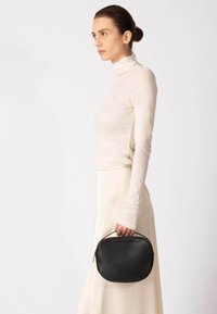 Sort læderhåndtaske med en rund form, glat tekstur og et håndtag. Designet har lynlås som lukning og diskrete syninger som detalje.