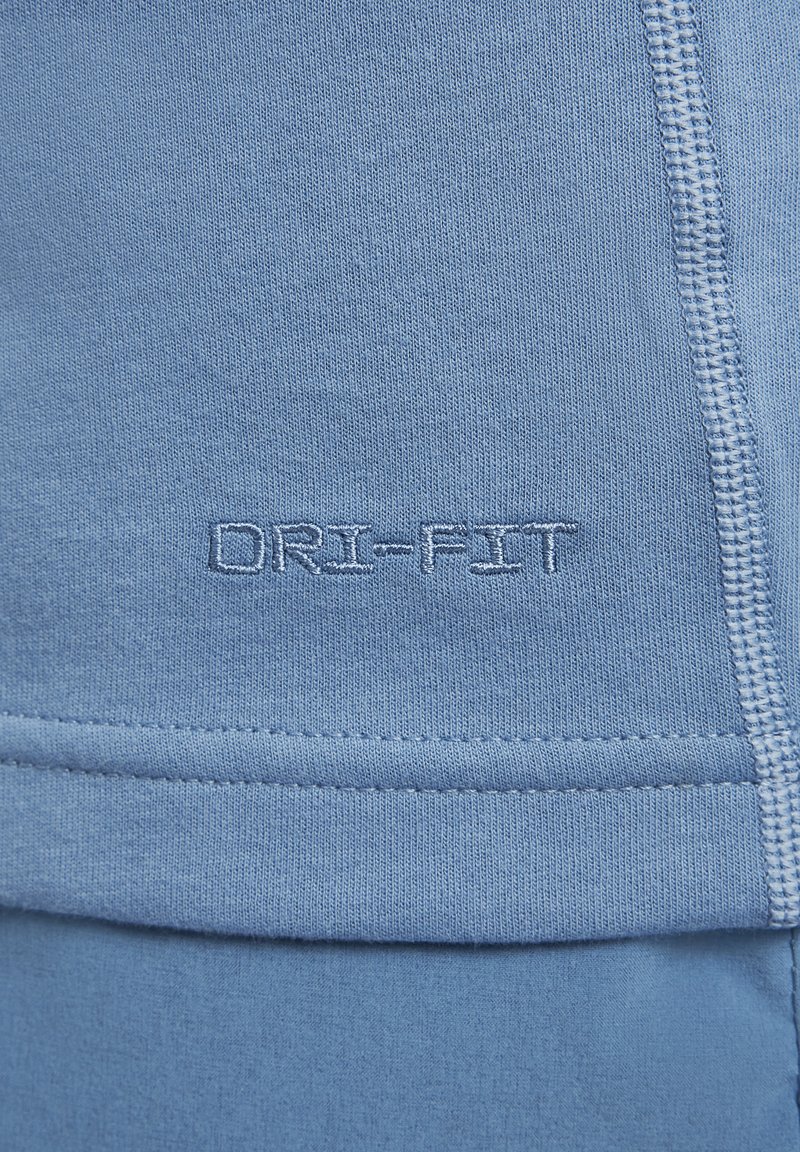 Jasnoniebieska tkanina Dri-Fit o gładkiej fakturze; posiada przeszyty dołek i detale z logo. Prosty design, bez wzorów i akcentów.