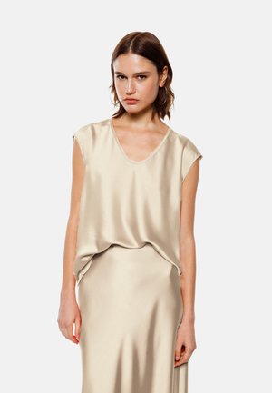Top in satin beige con scollatura a V profonda e maniche corte, che drappeggia delicatamente sul corpo. Texture liscia con dettagli di design minimi.