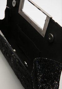 Mustan käsilaukun sisus, jossa on sileä kangasvuori, metallinen runko ja pieni tasku; sisältää kimaltavan rakenteen ja hienovaraisia kuvioita.