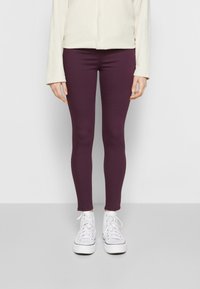 Leggings ajustados en un púrpura profundo, hechos de material elástico, combinados con zapatillas altas blancas y una blusa beige claro.