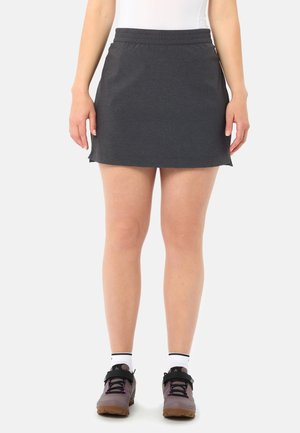 Unterkörper einer Person, die einen dunkelgrauen Sportrock, weiße Knöchelsocken und graue Wanderschuhe mit schwarzen Riemen trägt.