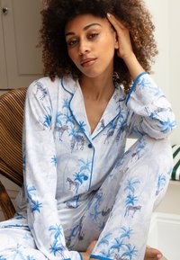 Witte pyjama set met blauwe palmbomen en zebrapatronen, voorzien van blauwe bies langs de kraag, knopen en mouwen. Lichtgewicht stof.