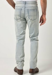 Vaqueros de mezclilla azul claro con corte recto, con dos bolsillos traseros y una textura ligeramente desgastada. Combinados con zapatos marrón oscuro.