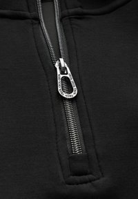 Schwarze Zip-Hoodie mit einem silbernen Reißverschluss und einem markierten Ziehband, glatter Stoffoberfläche und verstärkten Nähten am Saum.