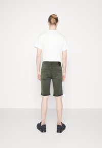 Olijfgroene shorts met een rechte snit, achterzakken en een zwarte tailleband, gecombineerd met een effen wit t-shirt en zwarte sneakers.