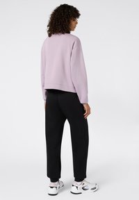 Sudadera corta en color lila combinada con pantalones joggers negros, que cuentan con puños elásticos y una textura suave. Lleva puesta unas zapatillas blancas y negras.