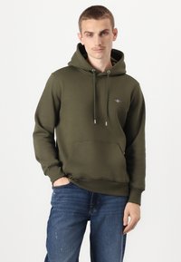 Oliven grønn hettegenser i myk stoff, med en frontlomme, snorer og en liten brodert logo på brystet.