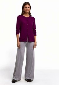 Lila Strickjacke mit Knöpfen und langen Ärmeln, kombiniert mit lockeren, grauen Hosen mit weitem Bein, getragen mit schwarzen Schuhen. Einfaches und sauberes Design.