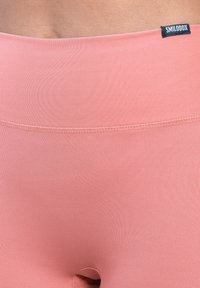 Leggings a vita alta di un rosa chiaro, realizzati in materiale elasticizzato con una consistenza liscia, dotati di un piccolo taglio e di un'etichetta nera in vita.