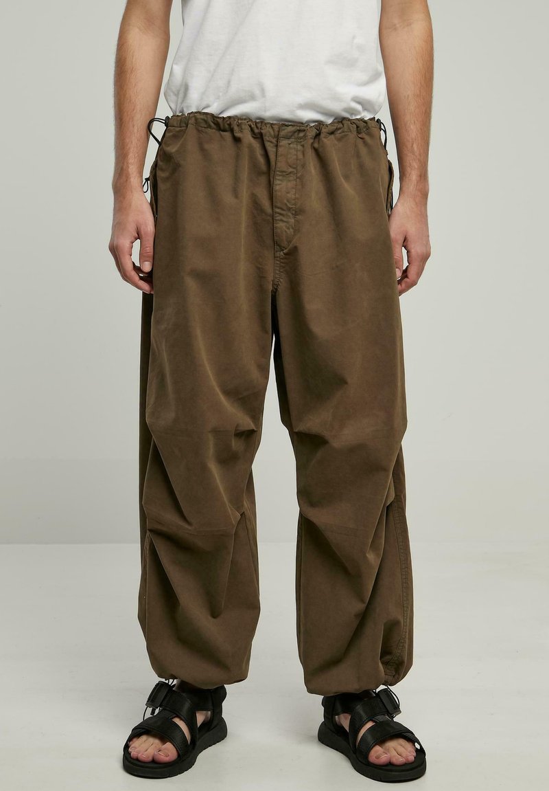 Brune bomuldsbukser med elastisk talje, justerbare snore og en løs pasform. Sammen med sorte sandaler, der har et minimalistisk design.