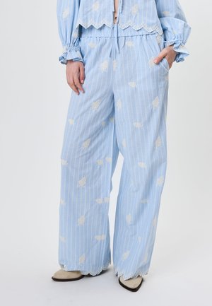 Hellblaue Hosen mit weitem Bein und weißen vertikalen Streifen, florale Spitzenstickerei, gewellte Säume, kombiniert mit passendem Oberteil und beigen spitzen Schuhen.