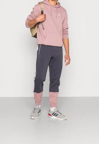 Pink hoodie with drawstrings and front pocket, paired with dark gray sweatpants featuring pink cuffs and white side stripes. Grey sneakers.