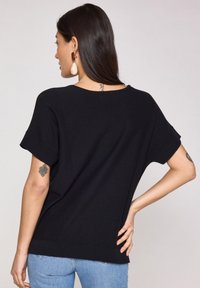 Maglietta nera a maniche corte con una vestibilità ampia, scollatura rotonda e texture lavorata a maglia. Presenta sottili spacchi laterali e polsini a coste.