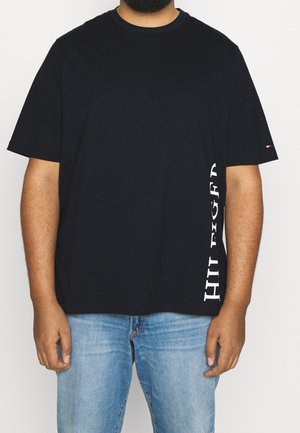 Camiseta de algodón negra con mangas cortas, con la palabra "HILFIGER" impresa en blanco en el lado izquierdo y un pequeño logo decorativo en la manga.