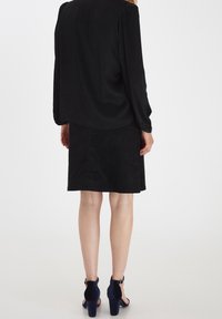 Černá halenka s dlouhými rukávy v kombinaci s černou sukní. Mezi vlastnosti patří hladká textura a jednoduchý design. Vysoké podpatky v námořnické modři.