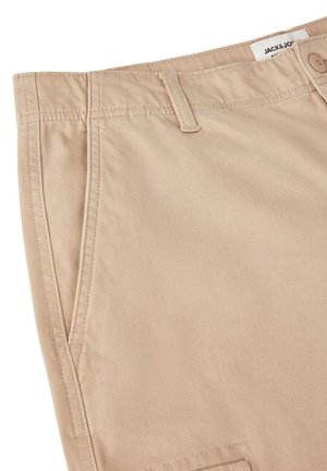 Beige katoenen broek met een soepele textuur, voorzien van steekzakken, een ritssluiting met knoop, en subtiele stikdetails.
