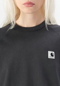 Sweatshirt noir en coton, avec un col rond, des manches raglan et un logo en patch carré blanc sur la poitrine gauche.