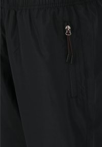 Pantalones ligeros negros con cintura elástica, que cuentan con un bolsillo lateral con cremalleras y una textura suave y mate.