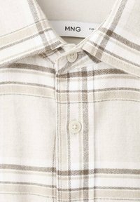 Weißes Baumwollhemd mit braunem Karomuster, versehen mit einem Button-Down-Kragen und einem einzigen Knopfverschluss an der Vorderseite.