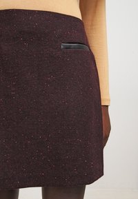 Jupe bourgogne en tissu texturé, ornée d'une poche en simili cuir noir, avec une coupe ajustée et un motif légèrement moucheté.