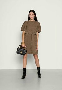 Vestido castanho com textura, de mangas curtas e encebadas, com uma cintura franzida, combinado com uma bolsa acolchoada preta e botas de tornozelo pretas.