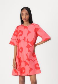 Short-sleeve dress made of lightweight fabric in bright pink, featuring large red floral patterns. Relaxed fit and round neckline.