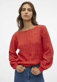 Lysrød ribbet sweater med lange, puffede ærmer og en bred halsudskæring, parret med en denimskørt. Teksturen ser blød og strikket ud.