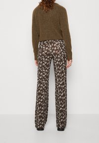 Hnědé široké kalhoty s květinovým vzorem, vyrobené z lehkého materiálu, nošeny s krátkým olivově zeleným svetrem.