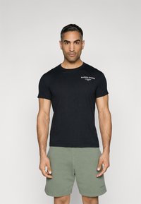 Zwart T-shirt met korte mouwen en ronde halslijn, voorzien van witte tekst op de borst. Gepaard met lichtgroene shorts. Soepele stoftextuur.