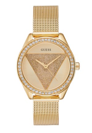 Orologio in metallo dorato con cinturino a rete, quadrante triangolare con texture sabbiosa e lunetta accentuata da pietre. Presenta lancette dorate e logo 'Guess'.