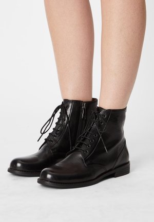 Des bottines en cuir noir pour la cheville, dotées d'un laçage à l'avant et d'une fermeture éclair sur le côté, avec un bout arrondi et une finition texturée. Talon bas empilé.