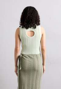 Muntgroene geribbelde mouwloze top met een ronde uitsnijding aan de achterkant, gecombineerd met een bijpassende gebreide rok met hoge taille en patroondetails.