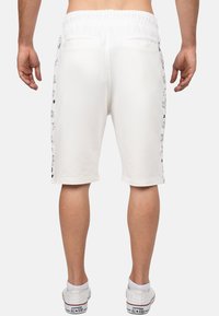 Pantaloni corti bianchi in cotone con elastico in vita, caratterizzati da stampe grafiche laterali e due tasche posteriori, tagliati poco sopra il ginocchio.
