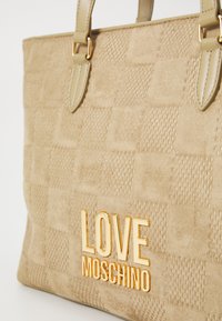Kreminė zomšinė pirkinių rankinė su tekstūruotu langelių raštu, auksinės spalvos "LOVE MOSCHINO" logotipu ir dviem rankenų diržais.