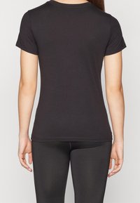 Camiseta negra de cuello redondo con mangas cortas, de tela suave, silueta ajustada, textura lisa y detalles sutiles de costura.