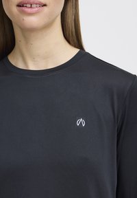 Must mustaga särk sujuvas kangas, millel on väike valge logo vasakus rinnas ja klassikaline ümmargune kaelus.
