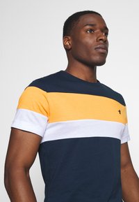 Short-sleeve t-shirt featuring horizontal stripes in navy, orange, and white. Made of cotton with a crew neckline and small logo detail.