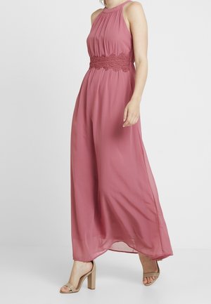 Woman wearing a sleeveless mauve maxi dress with lace waistband and pleated bodice, paired with beige high-heeled sandals.