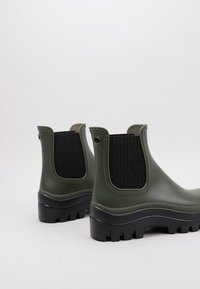 Botas de goma verdes hasta el tobillo con paneles laterales elásticos negros, suelas texturizadas y un acabado suave. Diseñadas para la durabilidad y la comodidad.
