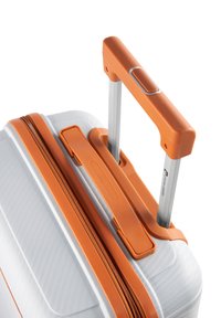 Maleta rígida blanca con acentos naranjas, que cuenta con un mango telescópico, superficie texturizada y cierre con cremallera.