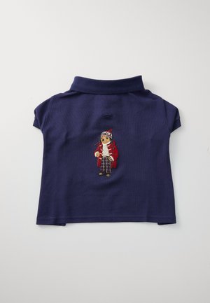 Polo de color azul marino con mangas cortas, que presenta un diseño bordado de una figura con abrigo rojo y pantalones decorados en el frente.