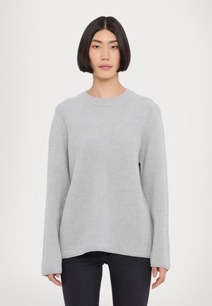Maglione grigio chiaro a coste con maniche lunghe e scollatura rotonda. Tessuto morbido; orli diritti; vestibilità rilassata. Indossato con jeans scuri.
