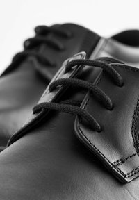 Czarne skórzane buty o gładkiej fakturze, z czarnymi sznurowadłami, okrągłym noskiem i szczegółowym przeszyciem w górnej części.
